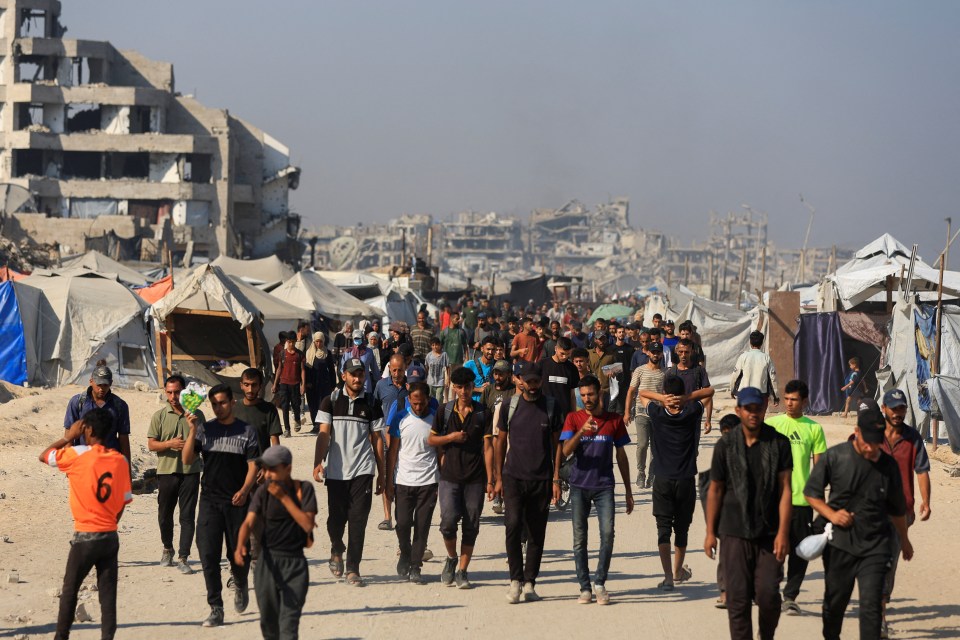 Palestinians walking near damaged buildings and tents in Gaza, waiting for aid.