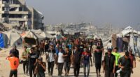 Palestinians walking near damaged buildings and tents in Gaza, waiting for aid.
