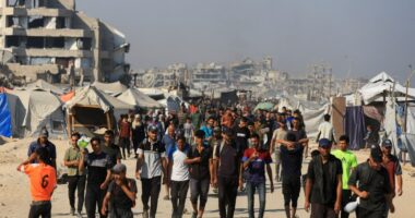 Palestinians walking near damaged buildings and tents in Gaza, waiting for aid.