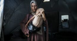 Malnourished child held by his mother in a tent.