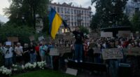 Protestors in Kyiv holding signs and a Ukrainian flag during a demonstration against a law reducing the powers of anti-corruption agencies.