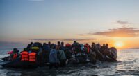 Migrants boarding a small inflatable boat at sunset.