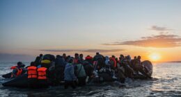 Migrants boarding a small inflatable boat at sunset.