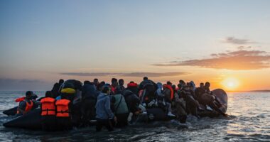 Migrants boarding a small inflatable boat at sunset.