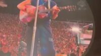 Chris Martin playing guitar on a large screen at a concert.
