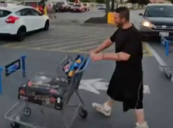 Man pushing a shopping cart in a parking lot.