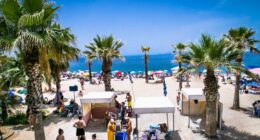 Crowded beach in Palaio Faliro, Athens, with palm trees and beach umbrellas.