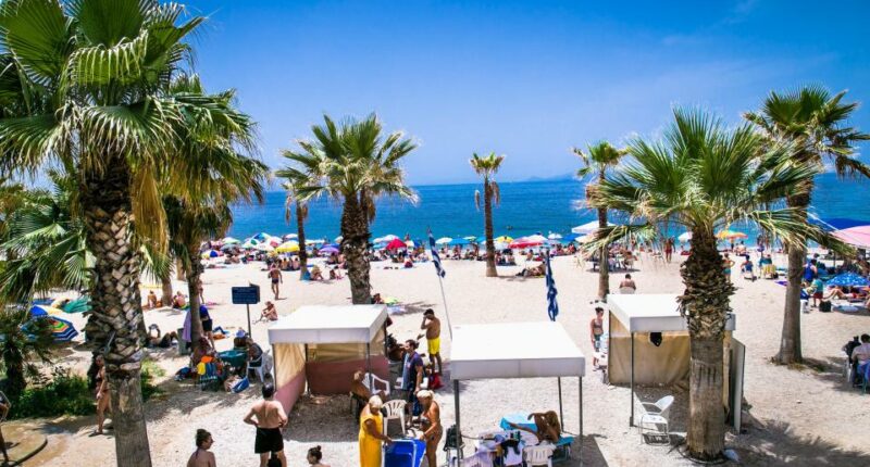 Crowded beach in Palaio Faliro, Athens, with palm trees and beach umbrellas.