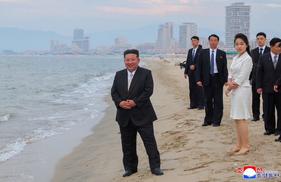 Kim Jong Un and his daughter on a beach with a city in the background.