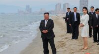 Kim Jong Un and his daughter on a beach with a city in the background.