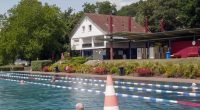 Outdoor pool with swimmers and a building in the background.
