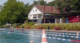 Outdoor pool with swimmers and a building in the background.