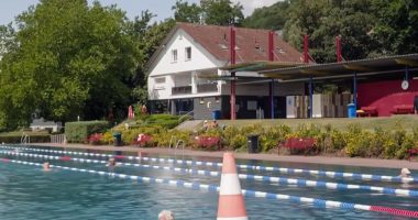 Outdoor pool with swimmers and a building in the background.