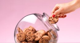 A hand taking a chocolate chip cookie from a cookie jar.