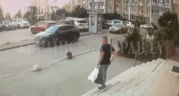 Man carrying a bag walks up steps towards a building with cars parked in the background.