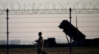 Soldier walking past Patriot air defense systems at a military hub.