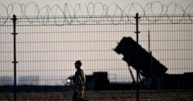 Soldier walking past Patriot air defense systems at a military hub.