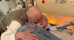 Man embracing a sick man in a hospital bed.
