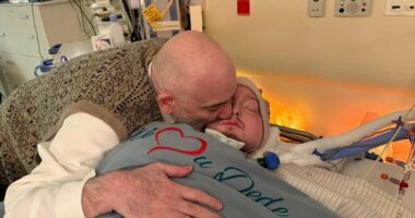 Man embracing a sick man in a hospital bed.