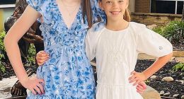 Two girls in dresses stand together near a statue.