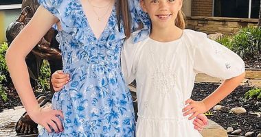 Two girls in dresses stand together near a statue.