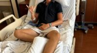Teenager in hospital bed with bandaged foot, giving shaka sign.
