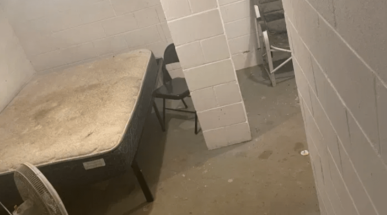 Basement room with mattress, fan, and chairs.