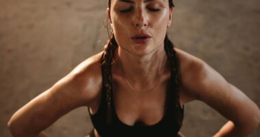 Fit woman with her hands on her hips taking deep breathe. Female athlete taking break after intense workout.