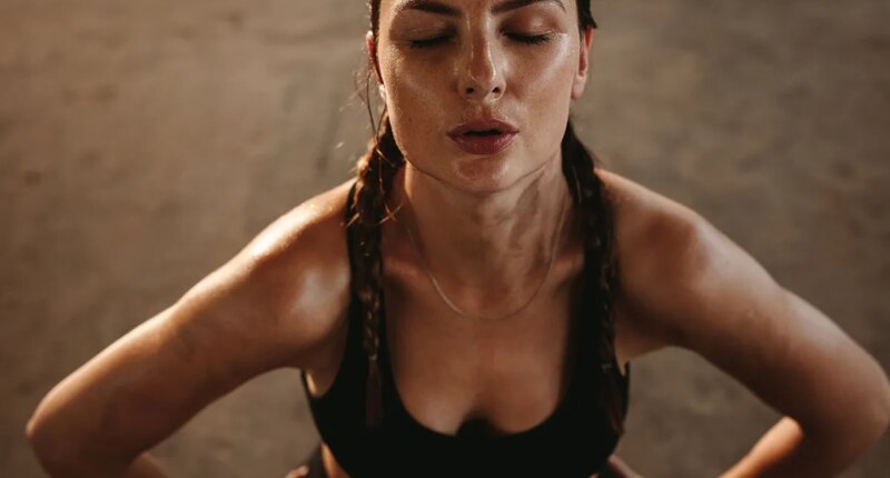 Fit woman with her hands on her hips taking deep breathe. Female athlete taking break after intense workout.