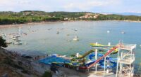 Aerial view of a beach with water slides and many boats.