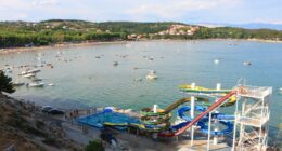 Aerial view of a beach with water slides and many boats.