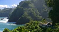 Car driving on a coastal road with ocean and cliffs.
