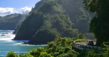 Car driving on a coastal road with ocean and cliffs.