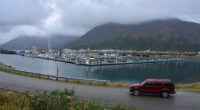 A red SUV drives past a harbor filled with fishing boats.