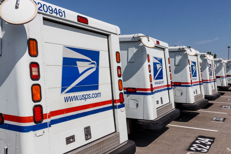 Rear view of several USPS mail trucks parked in a row.