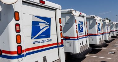 Rear view of several USPS mail trucks parked in a row.