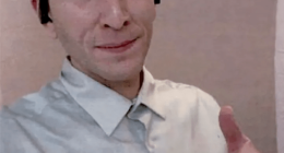 Man in a light gray shirt giving a thumbs up.