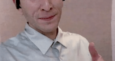 Man in a light gray shirt giving a thumbs up.