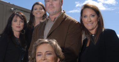 Group photo of five people, four women and one man, in front of a building.