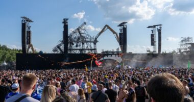 Crowd at Tomorrowland electronic music festival with damaged main stage being dismantled.
