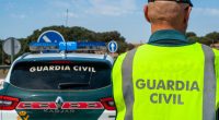 Spanish Civil Guard officer in reflective vest next to patrol car.