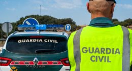 Spanish Civil Guard officer in reflective vest next to patrol car.