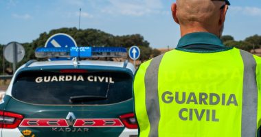 Spanish Civil Guard officer in reflective vest next to patrol car.
