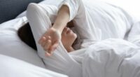 Sleepless young woman suffering from insomnia or nightmares close up, bad dreams, tired depressed female covering eyes with hands, lying on pillow in bed, feeling headache or migraine