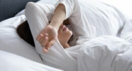 Sleepless young woman suffering from insomnia or nightmares close up, bad dreams, tired depressed female covering eyes with hands, lying on pillow in bed, feeling headache or migraine