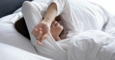 Sleepless young woman suffering from insomnia or nightmares close up, bad dreams, tired depressed female covering eyes with hands, lying on pillow in bed, feeling headache or migraine