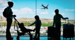 mother with kids and luggage looking at planes in airport, family travel