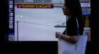 A pedestrian walks past a TV screen displaying a tsunami warning