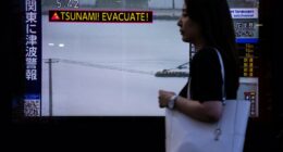 A pedestrian walks past a TV screen displaying a tsunami warning