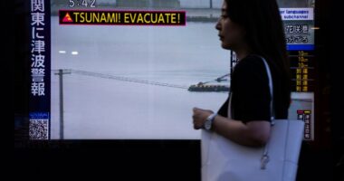 A pedestrian walks past a TV screen displaying a tsunami warning